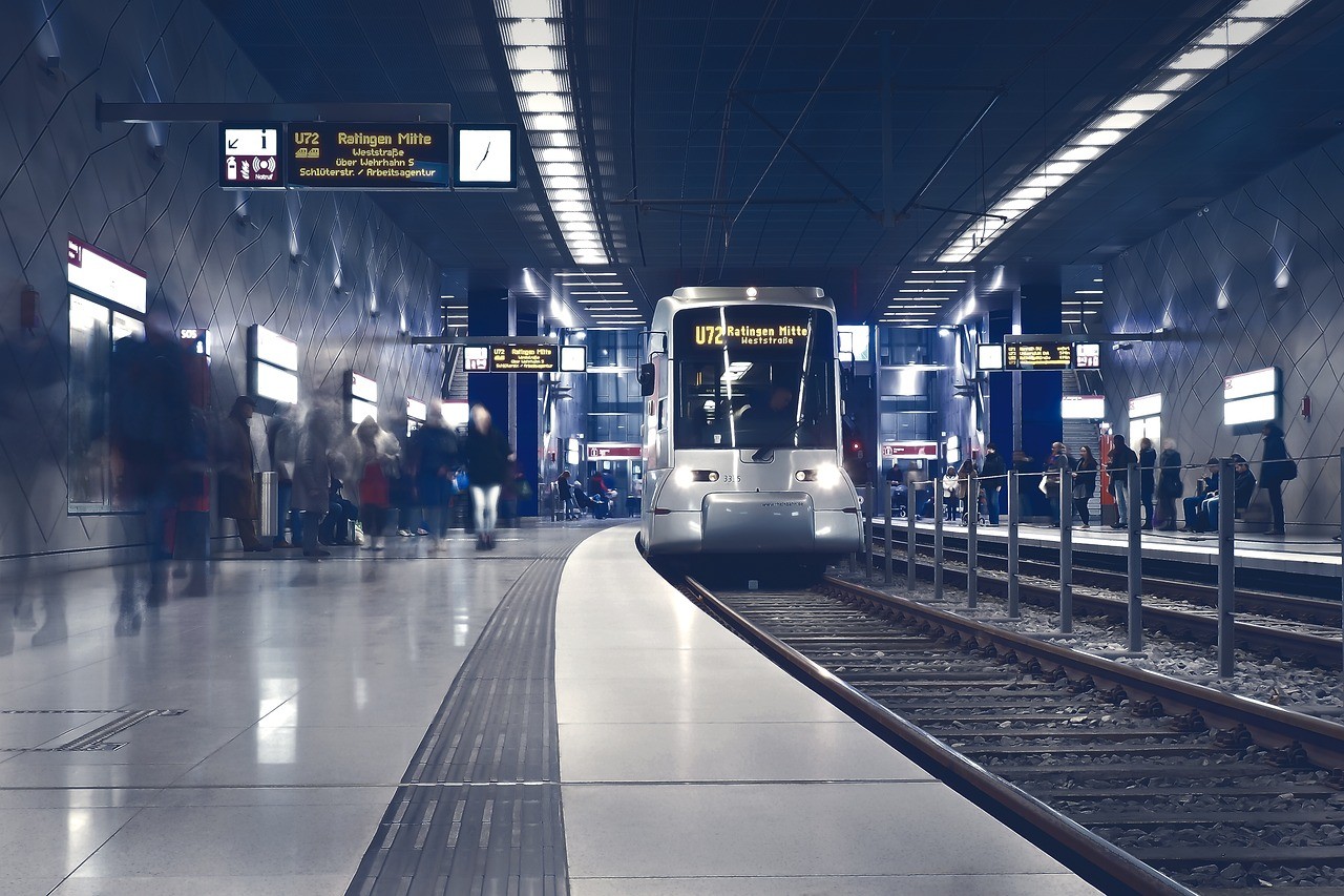 U-Bahn Station in die eine U-Bahn eingefahren ist. Von den Menschen sieht man auf dem Bahnsteig nur die Silhouetten.